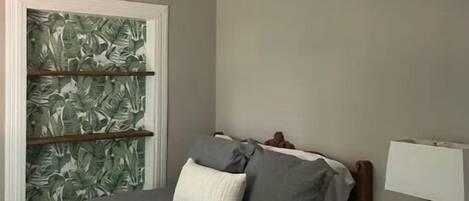 Een slaapkamer met een bed, nachtkastje, lamp, wandplank en plafondlamp.