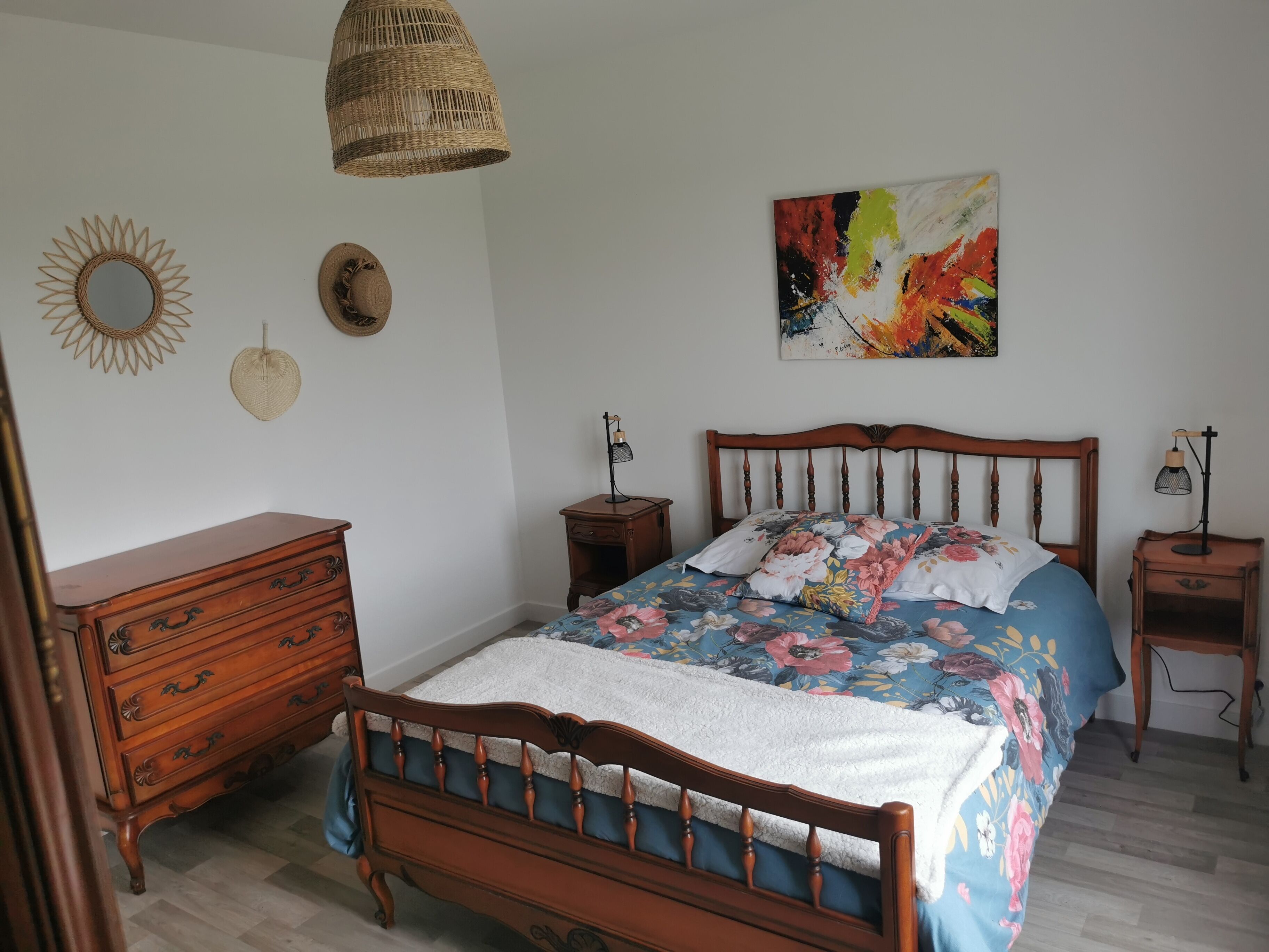 Un dormitorio con cama de madera, cómoda, mesita de noche, lámpara y una obra de arte en la pared.