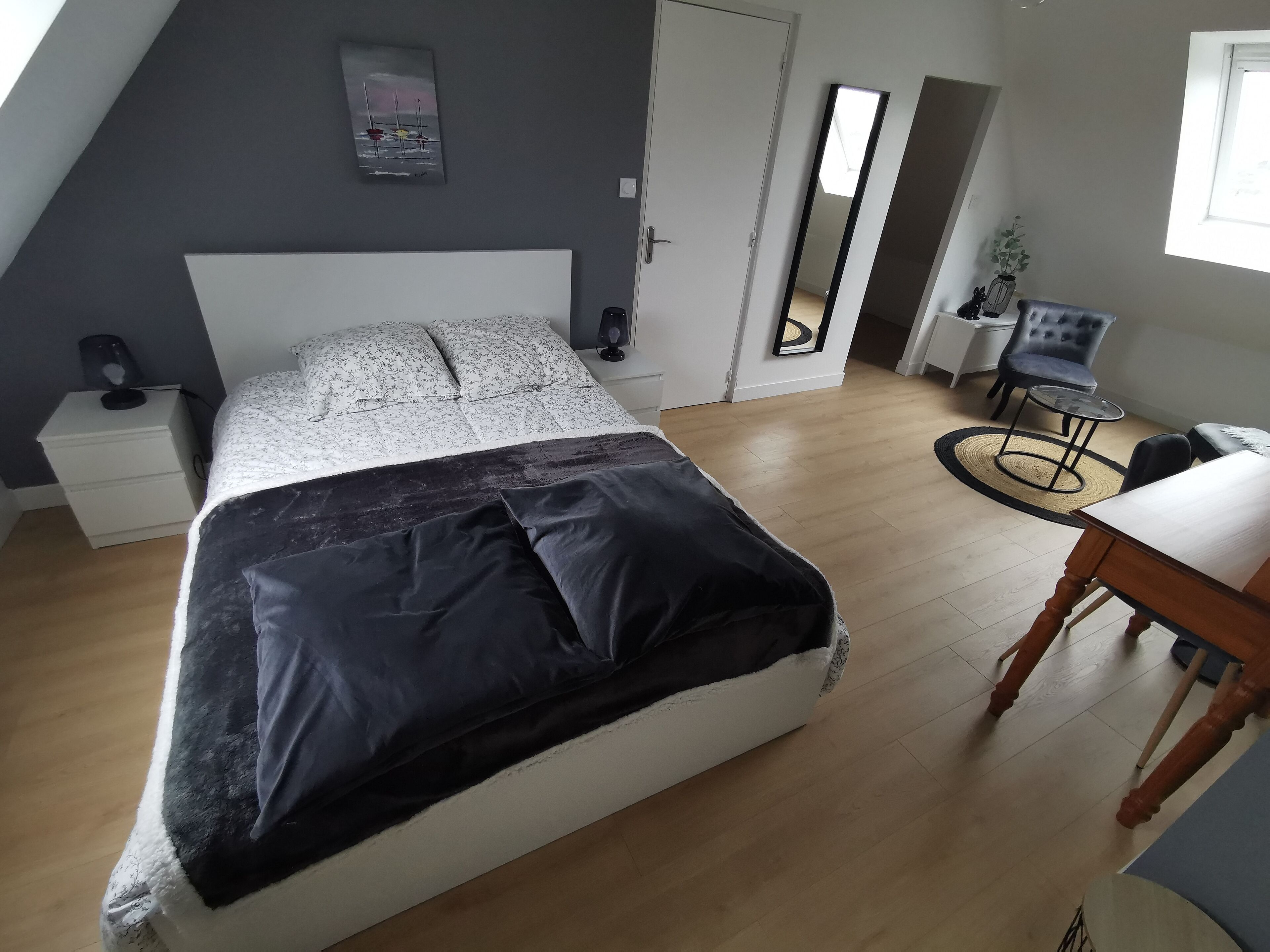 A bedroom with a bed, a nightstand, a desk, a chair, and a mirror.