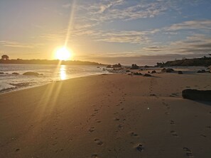 A beach with footprints leading to the water, a sunset in the background, and rocks scattered along the shore. - House by the Sea/Gîte (kerlouan)