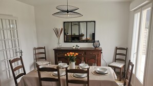 En matplats med ett bord dukat för fyra personer, omgiven av trästolar med vadderade sitsar. En vas med blommor står på bordet, och en spegel hänger på väggen ovanför.