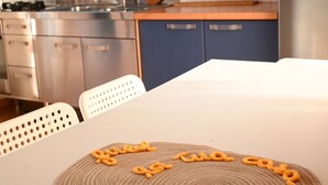 Et køkken med et hvidt bord, blå skabe og en rustfast stålvask.