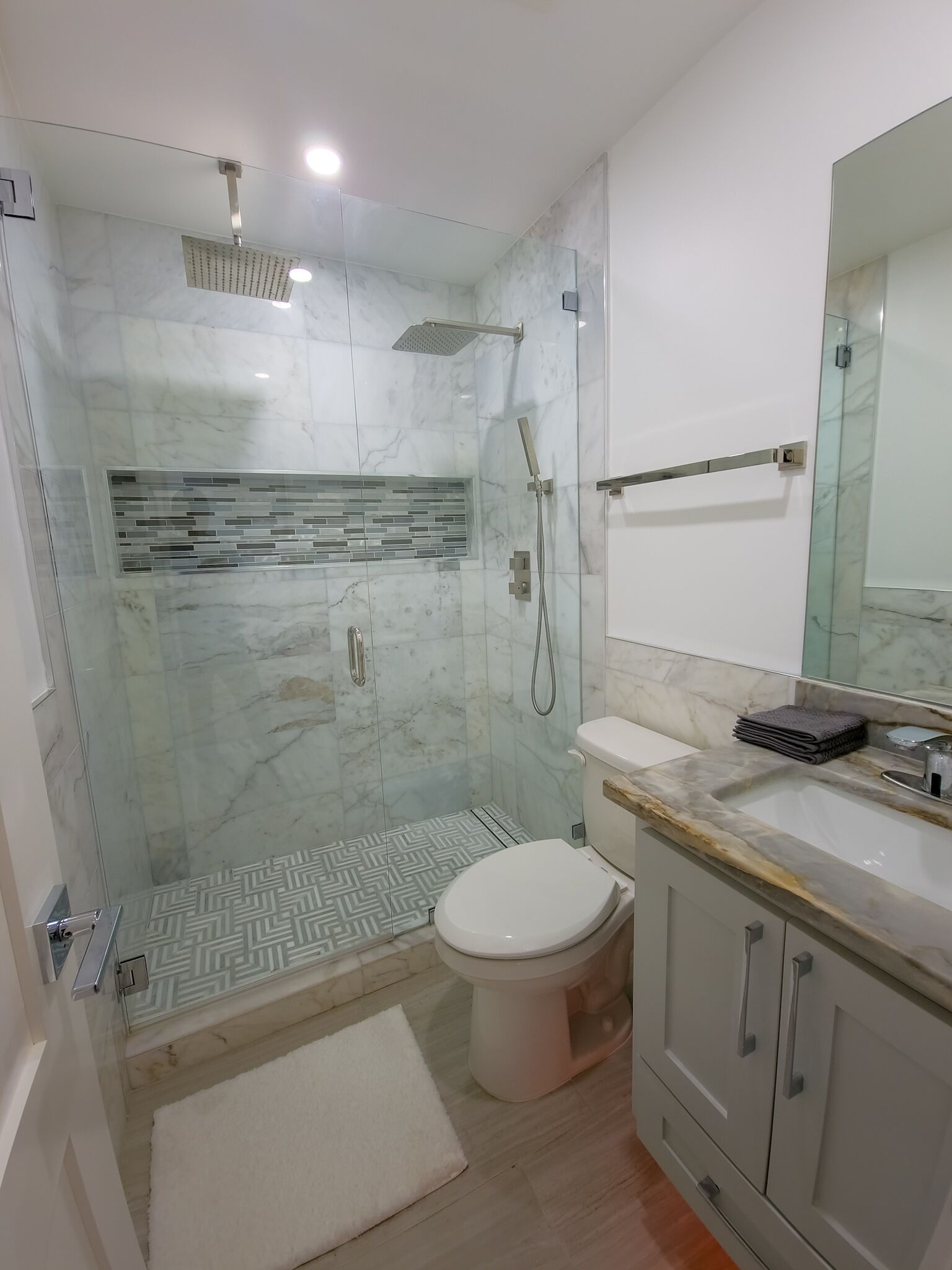 Une salle de bain moderne avec une douche à parois de verre, des toilettes et un meuble-lavabo avec un miroir.