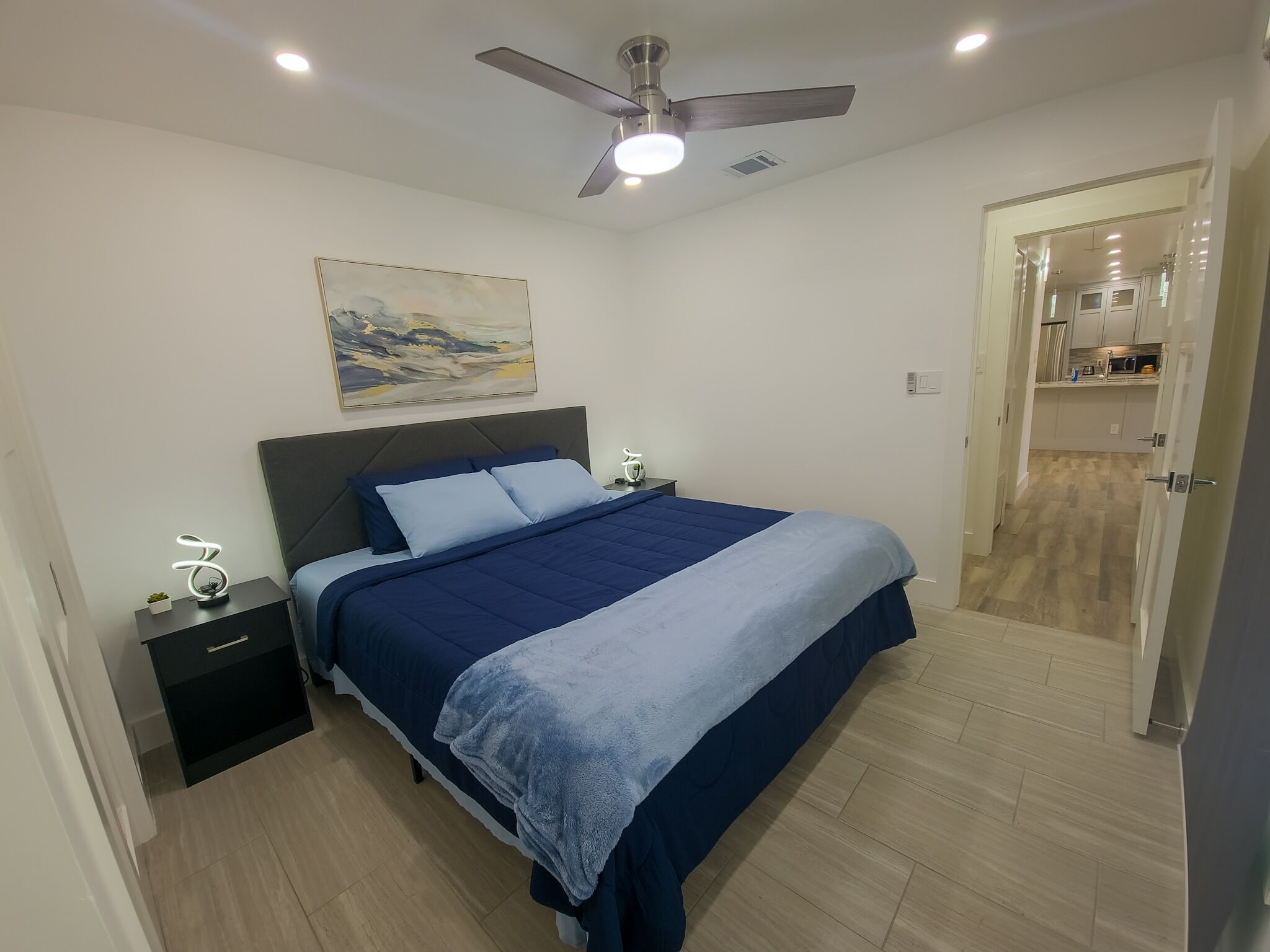 A bedroom with a bed, nightstands, a ceiling fan, and a painting on the wall.