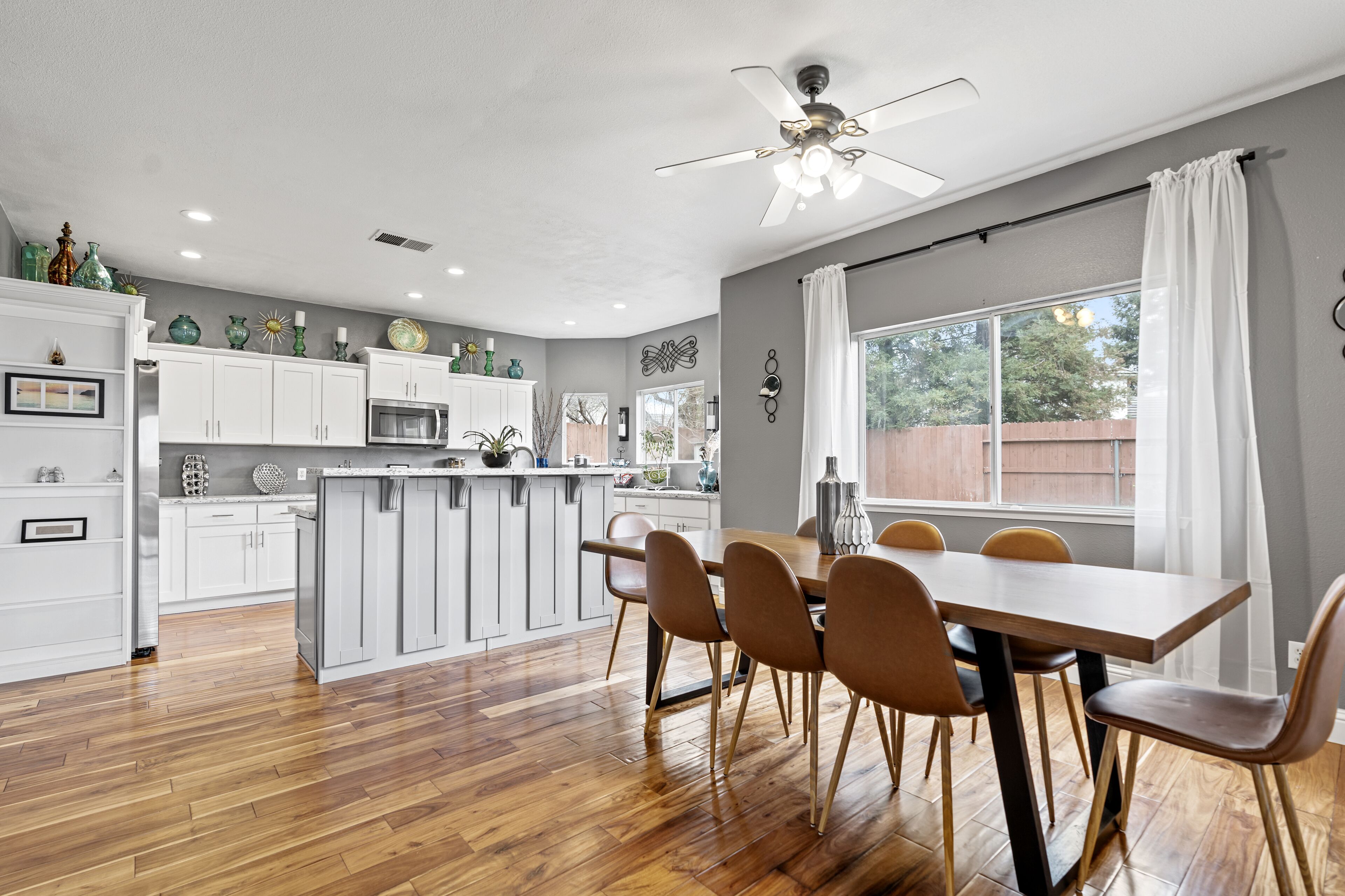 A modern kitchen with white cabinets, a central island, and a dining area with a wooden table and chairs.