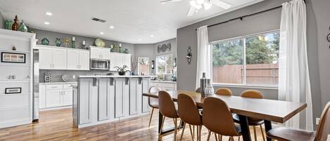A modern kitchen with white cabinets, a central island, and a dining area with a wooden table and chairs.