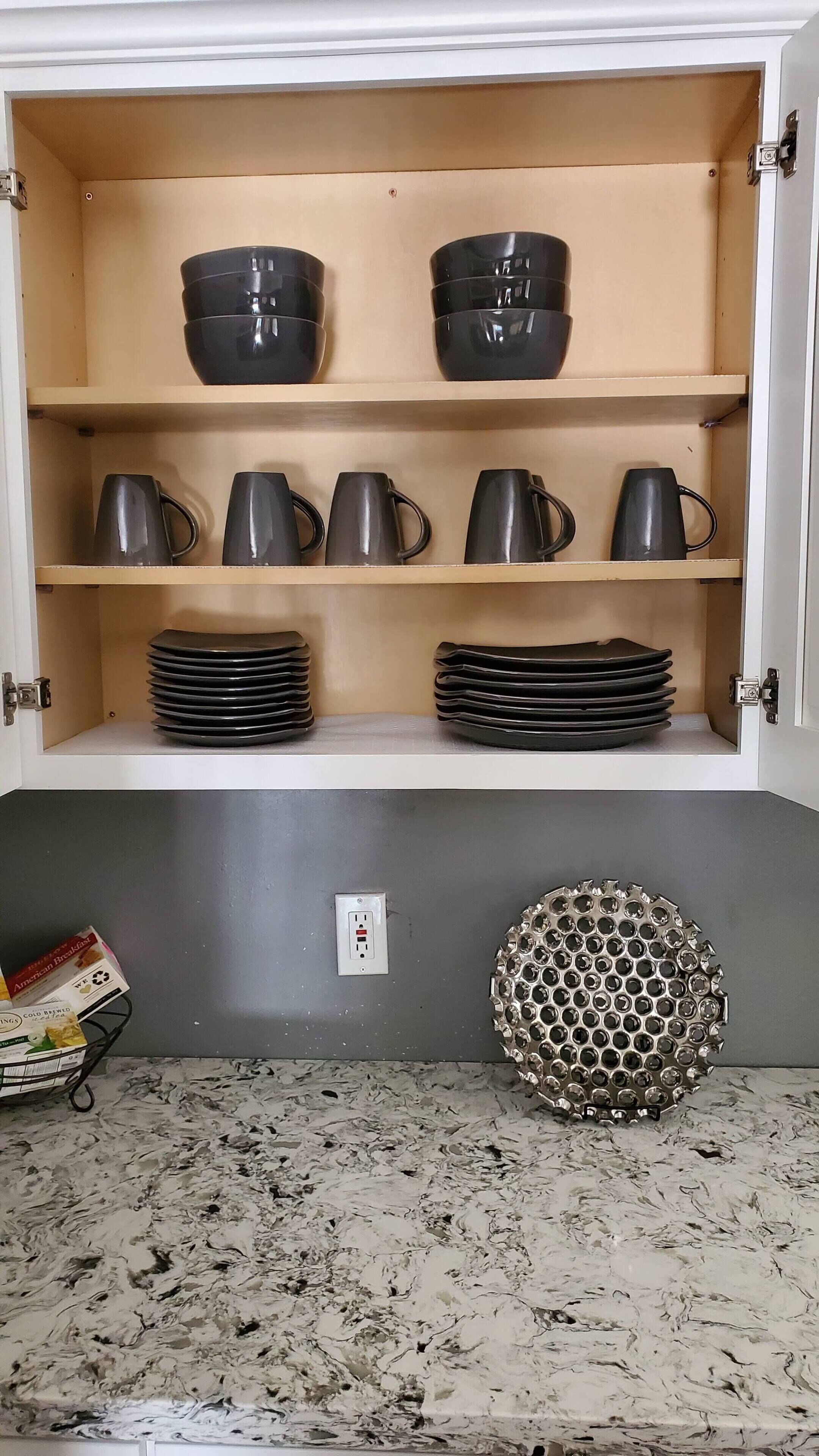 Un mueble de cocina con tazas y platos negros, un enchufe y una pieza decorativa de metal sobre la encimera.