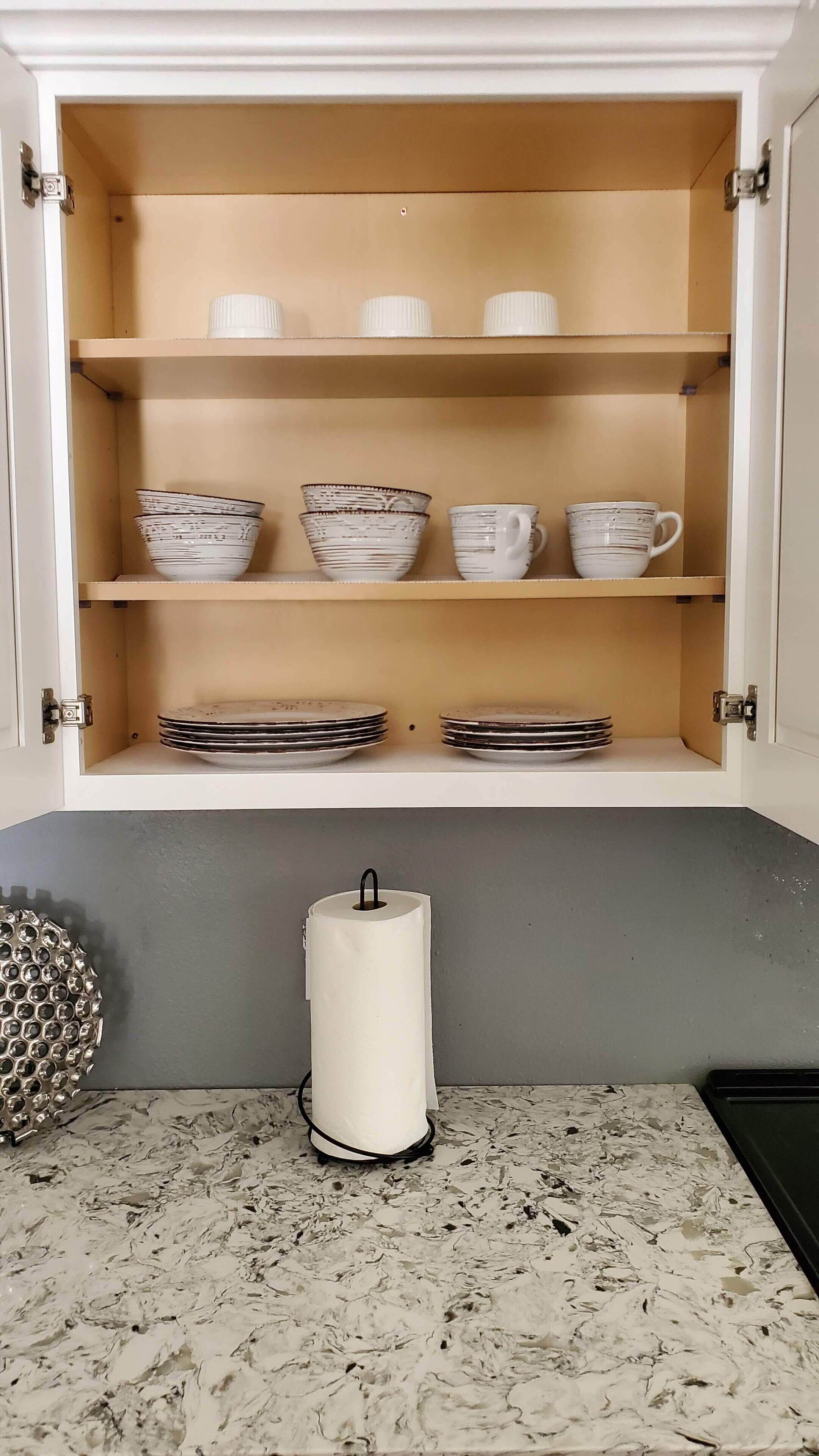Un meuble de cuisine avec des étagères où sont rangées des tasses blanches, des bols à rayures et des assiettes empilées.