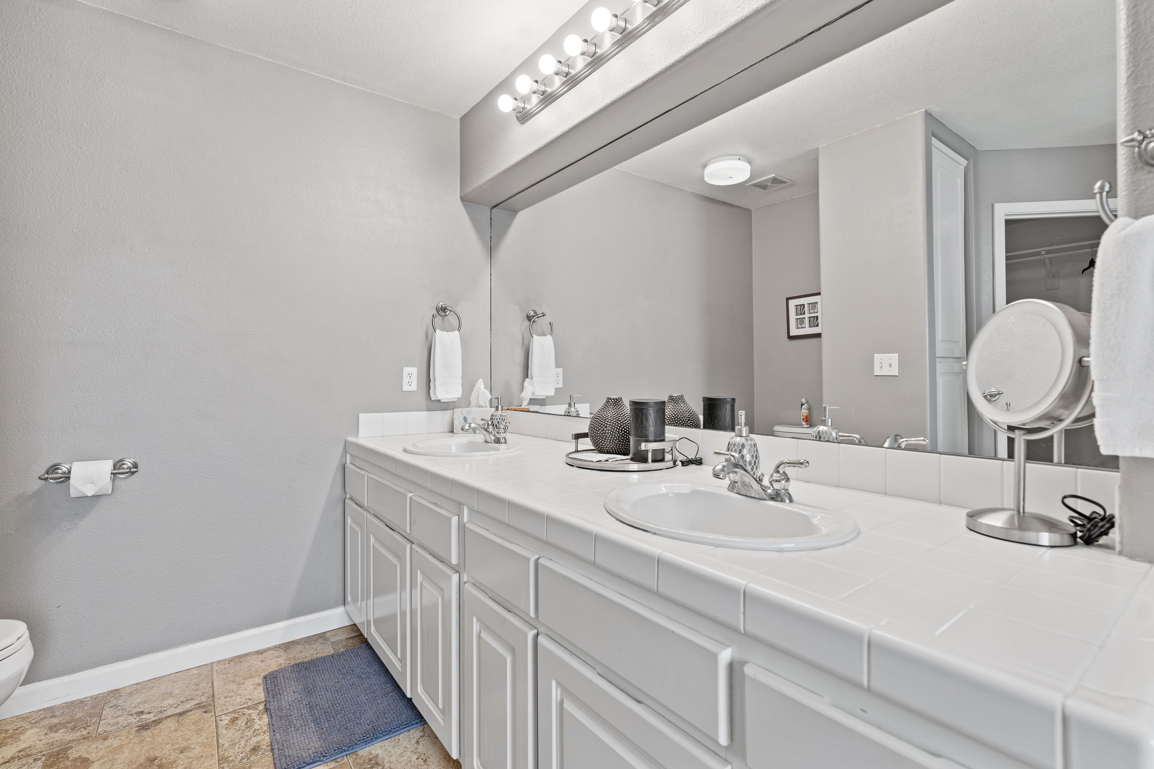 A modern bathroom with a large mirror, two sinks, and a toilet.