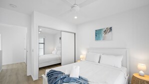 A modern bedroom with a large bed, a wardrobe, and a bedside table with a lamp. - Azure Riverside DeluxeTownhouse (Sunshine Coast)