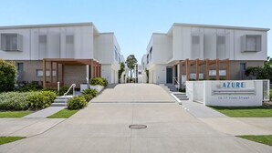 A modern apartment complex with a central walkway, wooden pergolas, and a sign indicating the name and address. - Azure Riverside DeluxeTownhouse (Sunshine Coast)