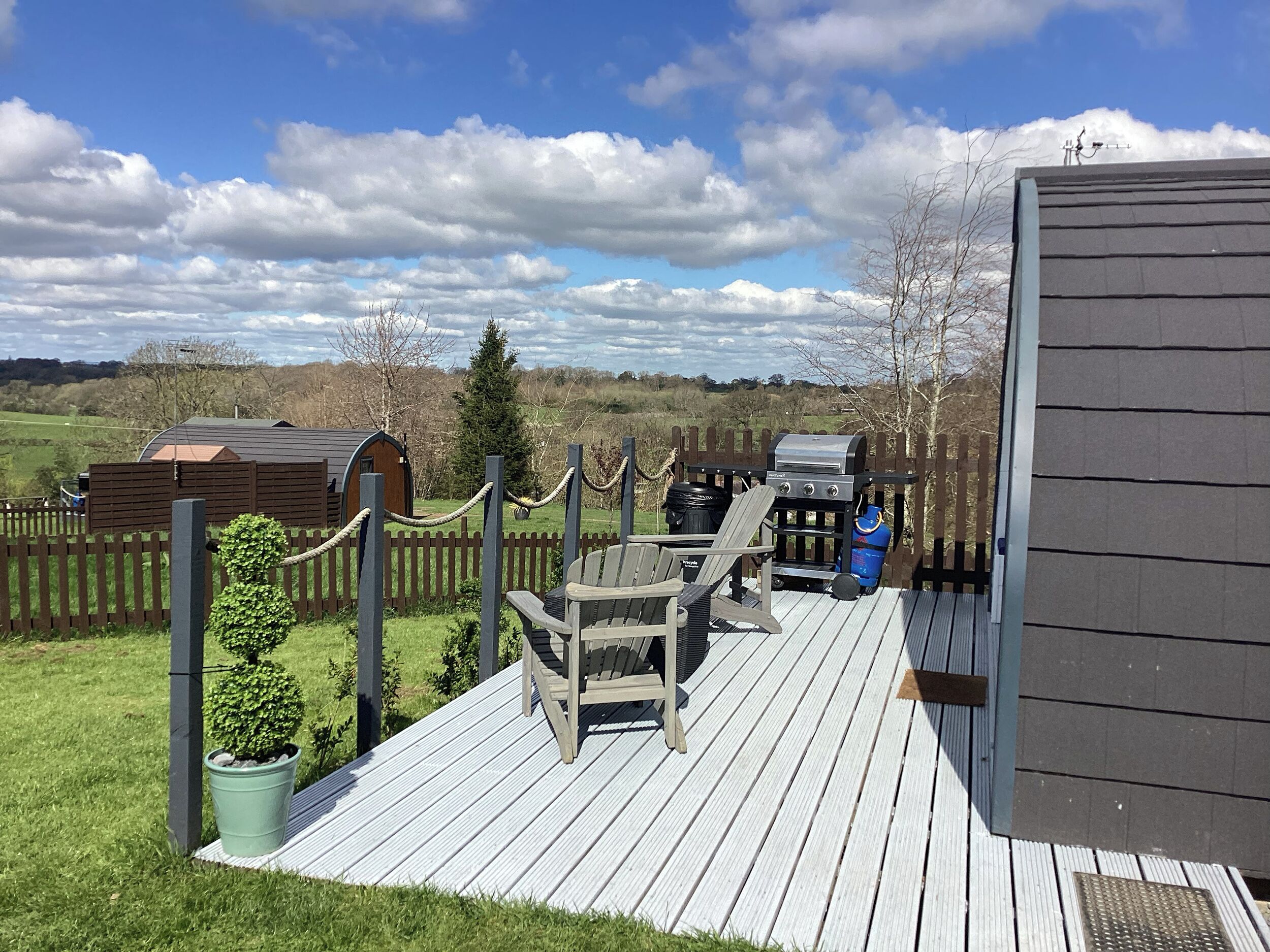 A deck with a grill, chairs, and a small shed.