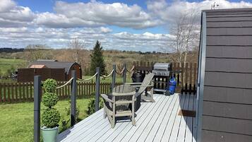 A deck with a grill, chairs, and a small shed.