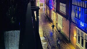 Uma rua estreita com edifícios em ambos os lados, alguns com janelas iluminadas.