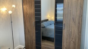 A bedroom with a wooden wardrobe, a bedside table with a lamp, and a bed with a blue quilt. - Spacious 3 bedroom house, 5 minutes to the beach, large garden, dogs welcome. (Newbiggin-by-the-Sea)