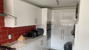 A modern kitchen with white cabinets, a red-tiled backsplash, a black toaster, and a built-in oven. - Spacious 3 bedroom house, 5 minutes to the beach, large garden, dogs welcome. (Newbiggin-by-the-Sea)