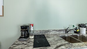 A kitchen with a built-in induction cooktop, a coffee maker, a jar of sugar, and a sink. - Peaceful Harvest Home in Hutto (hutto)