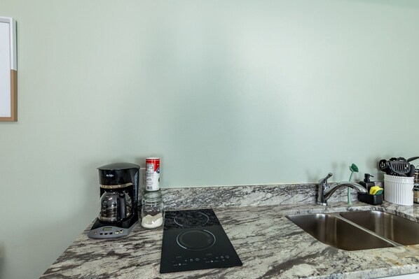 Een keuken met een geïntegreerd inductiekookveld, een koffiezetapparaat, een suikerpot en een spoelbak.