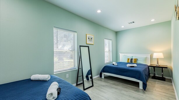 A hotel room with two beds, a mirror, a bedside table with a lamp, and a picture on the wall. - Peaceful Harvest Home in Hutto (hutto)