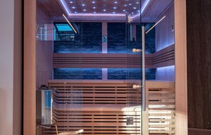 Una sauna con interior de madera, paredes de vidrio y un fondo de pared de piedra.