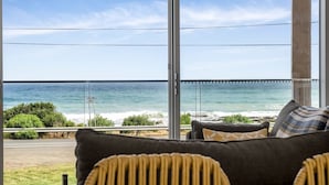 A room with a large window overlooking the ocean, a sofa with cushions, and a view of the beach and sea. - Six Degrees - Across the road from the Separation Creek beach (Separation Creek)