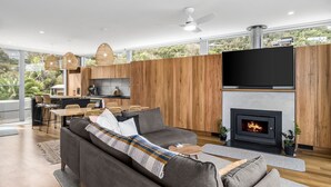 A modern living room with a fireplace, a dining area with a view, and a kitchen with wooden paneling. - Six Degrees - Across the road from the Separation Creek beach (Separation Creek)