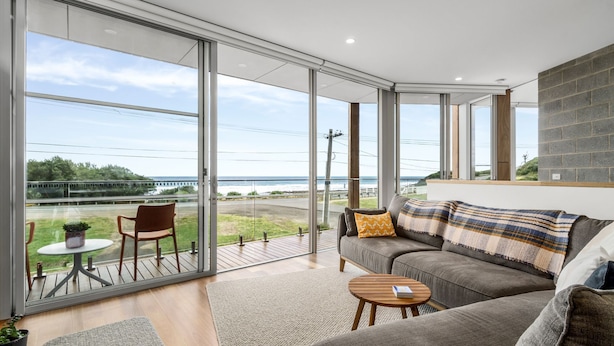 A modern living room with a large sliding glass door leading to a balcony overlooking a coastal view. - Six Degrees - Across the road from the Separation Creek beach (Separation Creek)