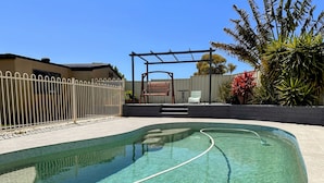 Una piscina cristalina con una valla blanca, una pérgola y un banco.