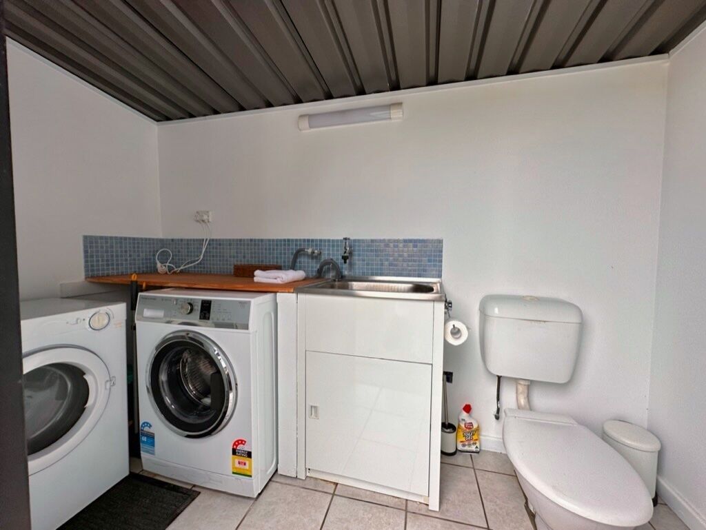 A compact kitchen with a washing machine, a sink, and a toilet.