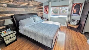 A bedroom with a wooden headboard, a bed with a grey quilt, a bedside table with a lamp, a wooden dresser, and a window with curtains. - Oasis w/Opt Heated Pool & Billiards- Mins to Strip (Las Vegas)