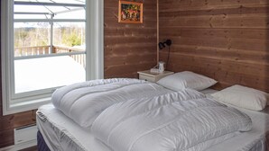 Un dormitorio con una cama grande, una mesita de noche con lámpara y una ventana con vistas a árboles y montañas.