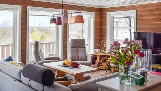 Un salón acogedor con sofá, sillón y mesa de centro. Hay un televisor en la pared y una ventana con vistas a árboles.