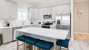 Una cocina moderna con armarios blancos, electrodomésticos de acero inoxidable y una isla central con taburetes de bar.