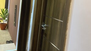 Un pasillo con dos puertas de madera oscura, una planta en maceta y piso de baldosas.
