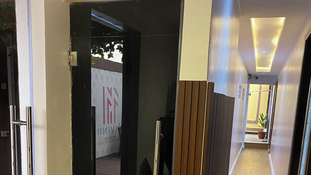 Un pasillo de hotel con piso de madera, una puerta de vidrio que da a una habitación y un letrero con el nombre del hotel.