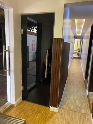 Een hotelgang met een houten vloer, een glazen deur naar een kamer, en een bord met de naam van het hotel.