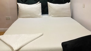 Una cama con cabecera capitonada, ropa de cama blanca y una toalla blanca doblada sobre la cama.