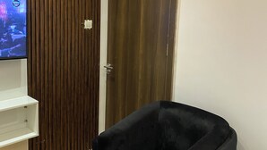 Una habitación con un armario de madera, un sillón negro y un televisor sobre una estantería blanca.