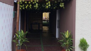 Entrada de un edificio con un letrero con el número 6, un corredor techado y plantas en macetas.