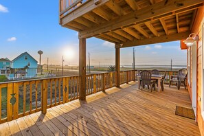 A wooden deck with a railing, a table, and chairs. - Ocean & Bay Views, Steps To The Beach, EV Charging, LG Fenced Yard, Fire Pit (Surfside Beach)