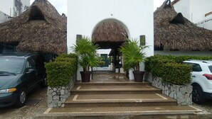 Une entrée d’immeuble avec un toit de chaume, des marches menant à un espace abrité et des plantes en pot de chaque côté.