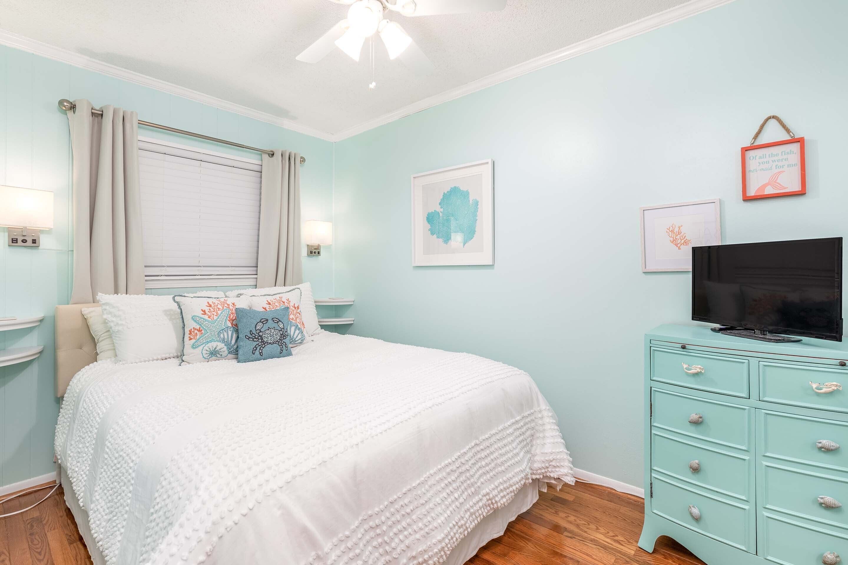A bedroom with a bed, a dresser, a ceiling fan, and wall art.