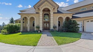 A two-story house with a symmetrical facade, a central entrance with a decorative arch, and a well-maintained lawn. - Beautiful Country Villa on 5 acres, 5 miles to downtown (Spokane)
