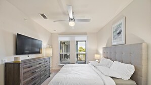 A bedroom with a large bed, a TV mounted on the wall, a ceiling fan, and a balcony with a view of the outdoors. - Art house sawyer yards (Houston)