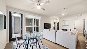 A modern living room with a glass dining table, two sofas, and a ceiling fan. - Art house sawyer yards (Houston)