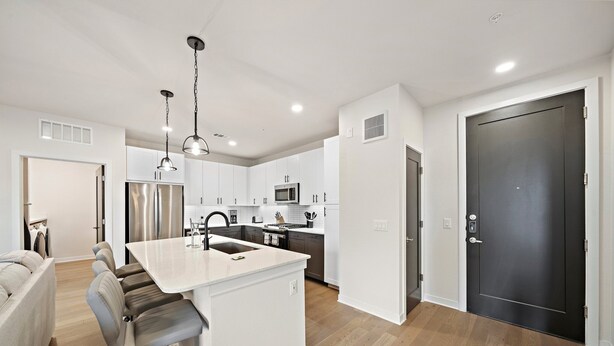 A modern kitchen with white cabinetry, stainless steel appliances, and a central island with bar stools. - Art house sawyer yards (Houston)