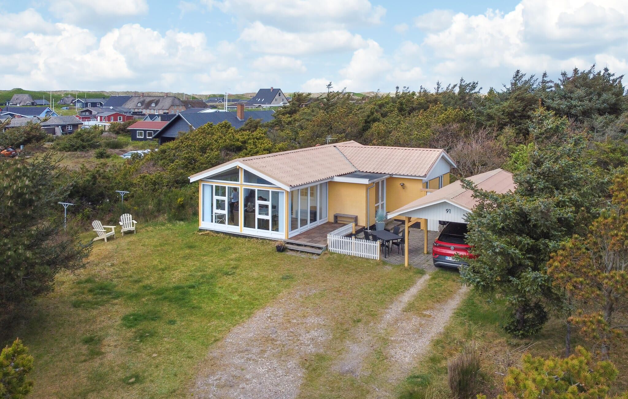 A single-story house with a large glass front, a covered porch, and a driveway leading to a parked car.