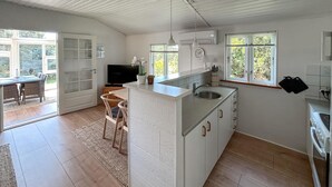A modern kitchen with a central island, a dining area with chairs, a TV, and a large window. - 2 bedroom gorgeous home in Ulfborg (Ulfborg)