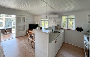 Une cuisine moderne avec un îlot central, un coin repas avec des chaises, un téléviseur et une grande fenêtre.