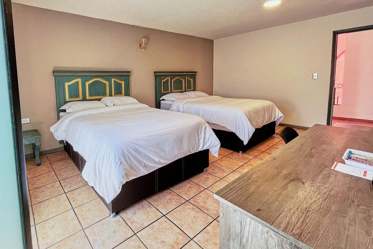 A hotel room with two beds, a wooden desk, and a tiled floor.